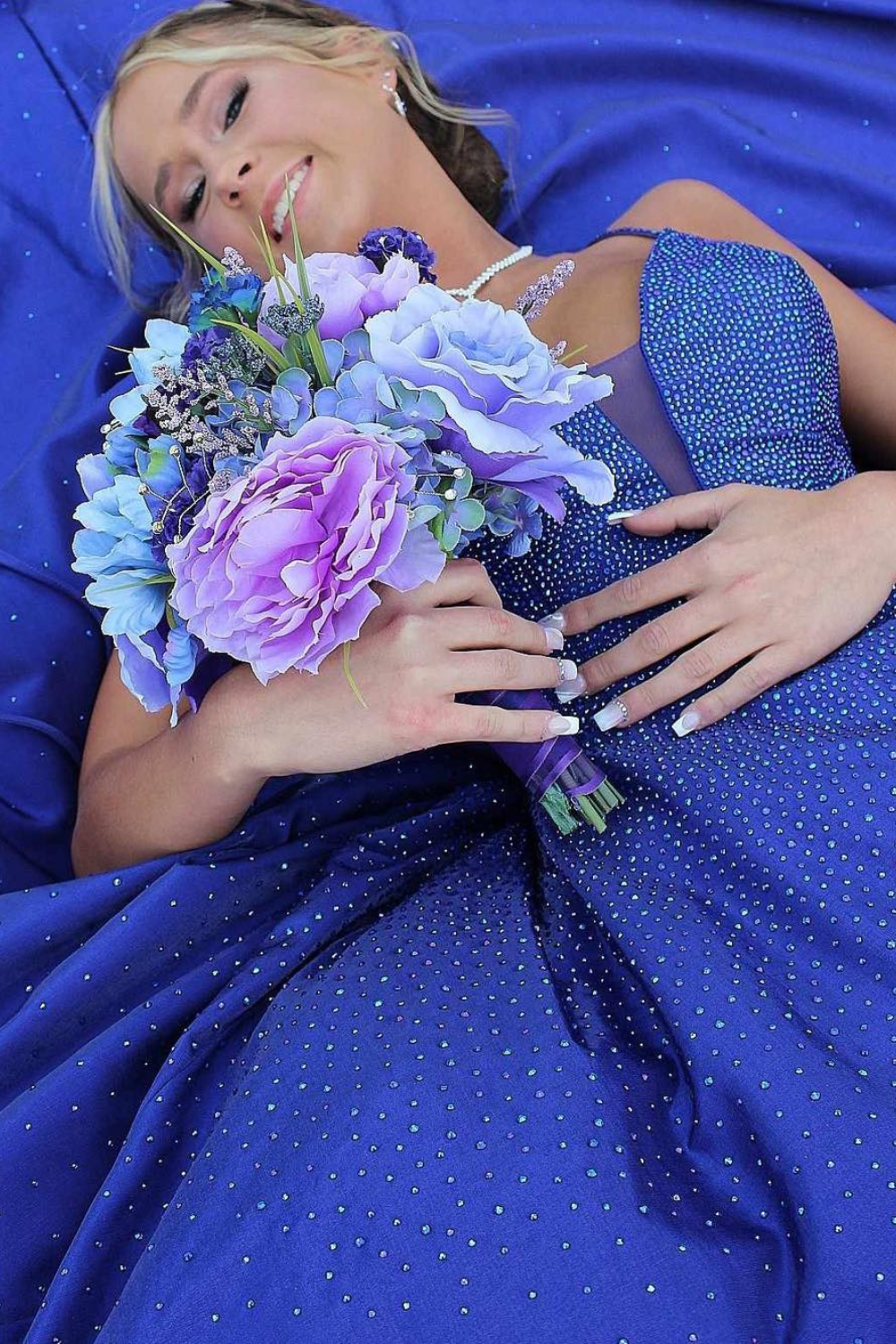 A close up photo of a girl laying back surrounded by her prom dress and holding a bouquet of flowers.
