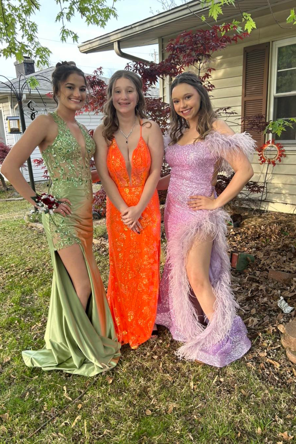 Three girls standing from left to right, wearing a green, orange and purple prom dress.