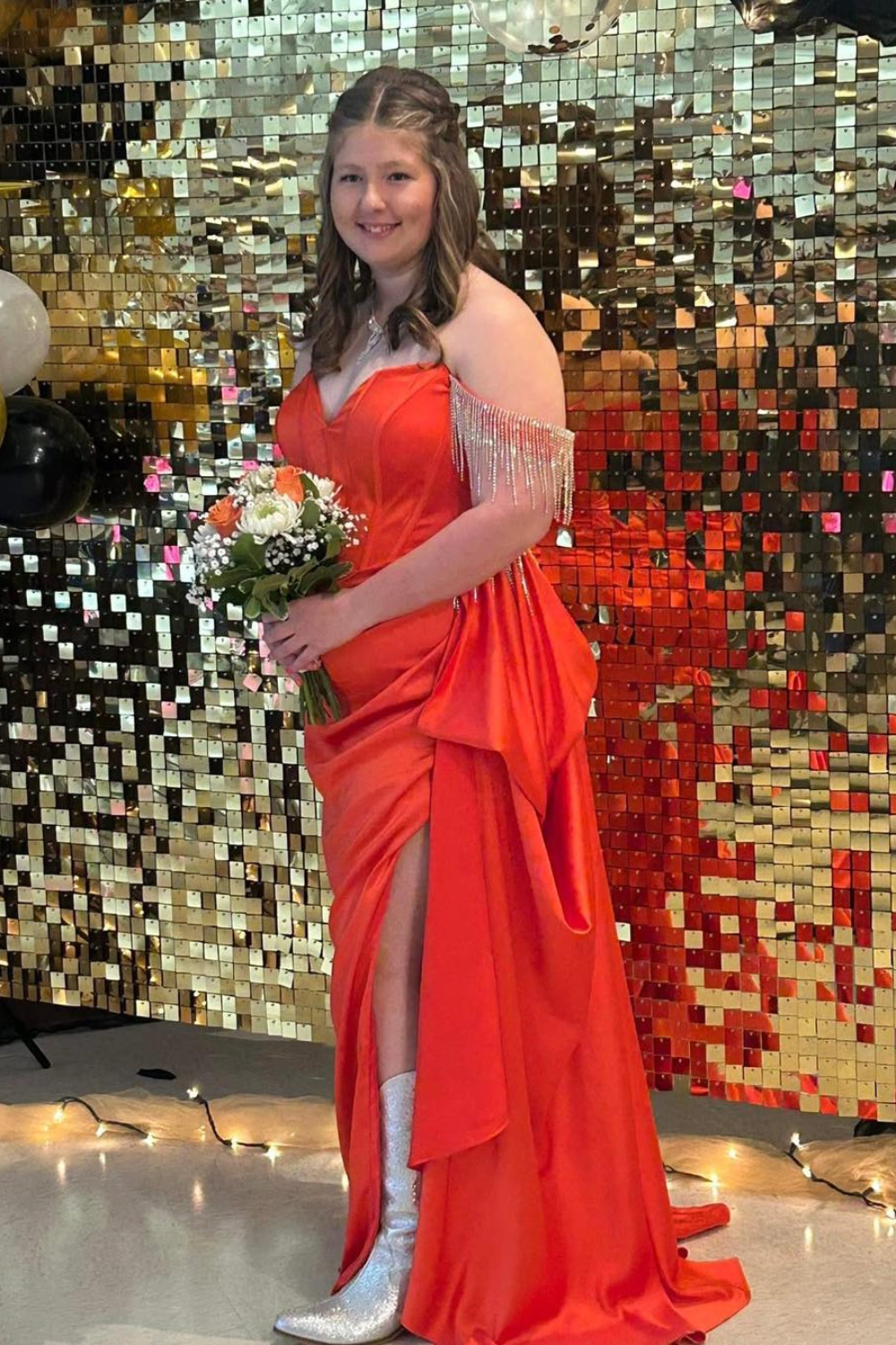 A girl in a red dress with a slit in the side standing in front of a gold disco background.