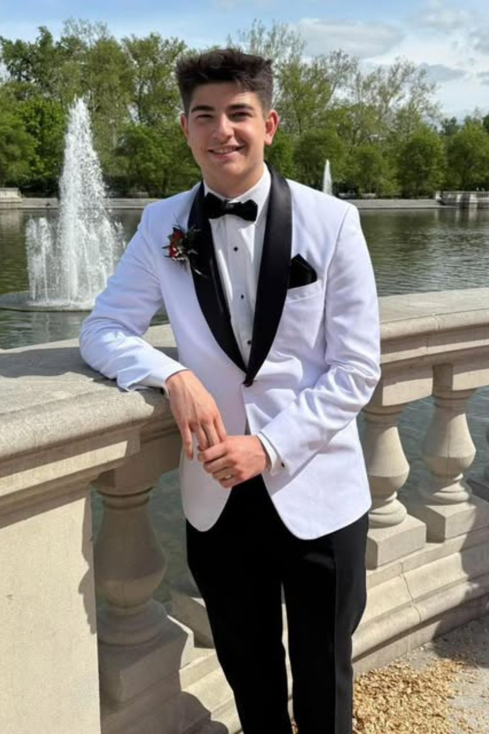 A boy standing with a white sprots coast and black pants.