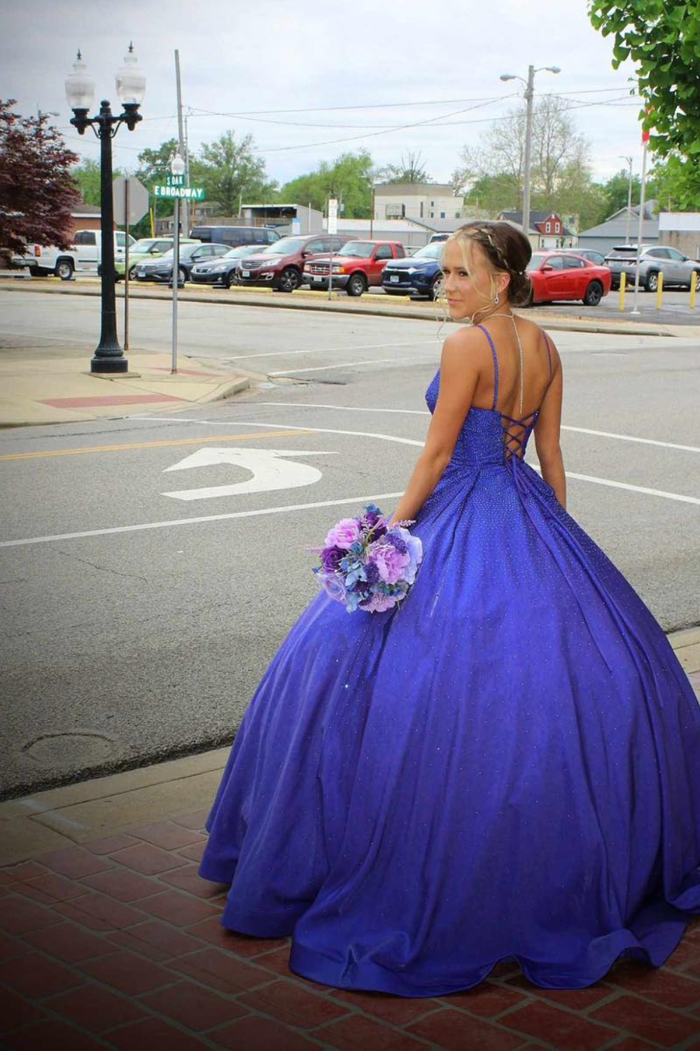 A girl in a blue dress standing at a highway intersection holding a bouquet of flowers.