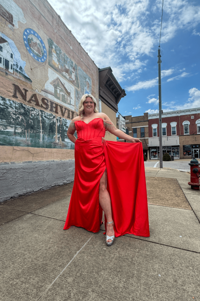 Home 1 Black Tie Affair model in bold orange gown holding out the train of her dress.