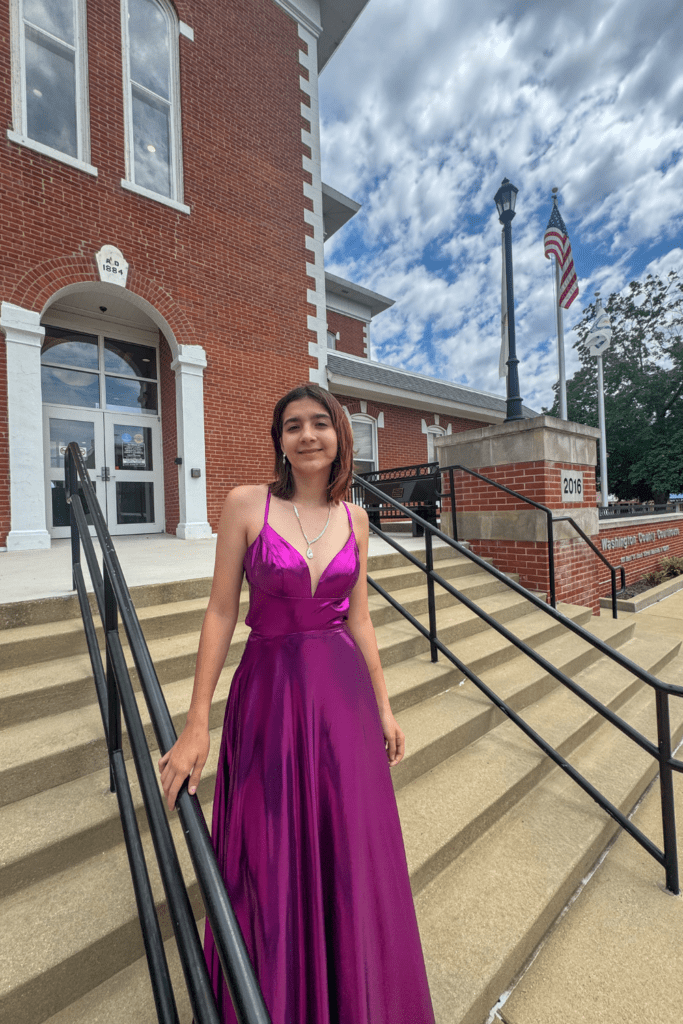 Home 2 Black Tie Affair model in purple gown with spaghetti straps standing on the steps.
